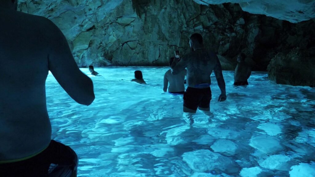 View inside the Blue Cave, located in Llovizi Bay. There are people swimming and taking pictures inside the cave.